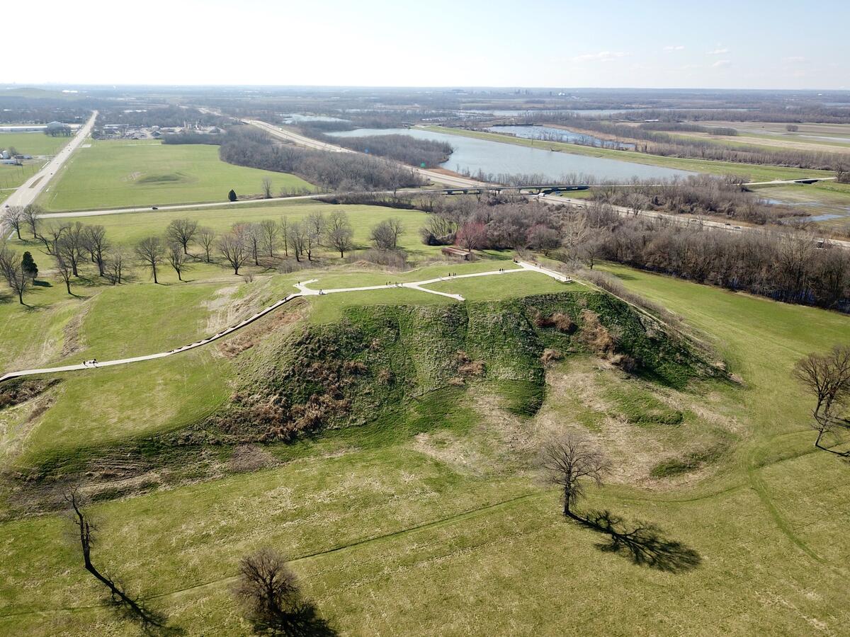 Aerial view of huge mound at Cahokia, surrounded by flat land with grass and trees, Mississippi river in distance