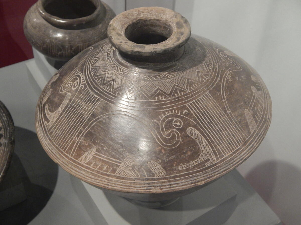 shiny dark brown ceramic vessel with bands of geometric designs covering the surface
