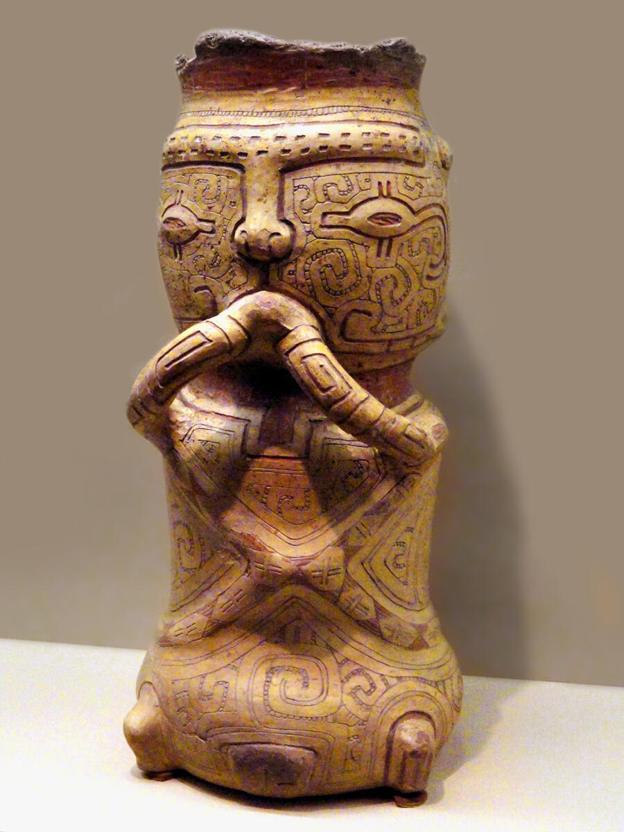 ceramic vessel in shape of a seated woman, decorated with detailed geometric designs.