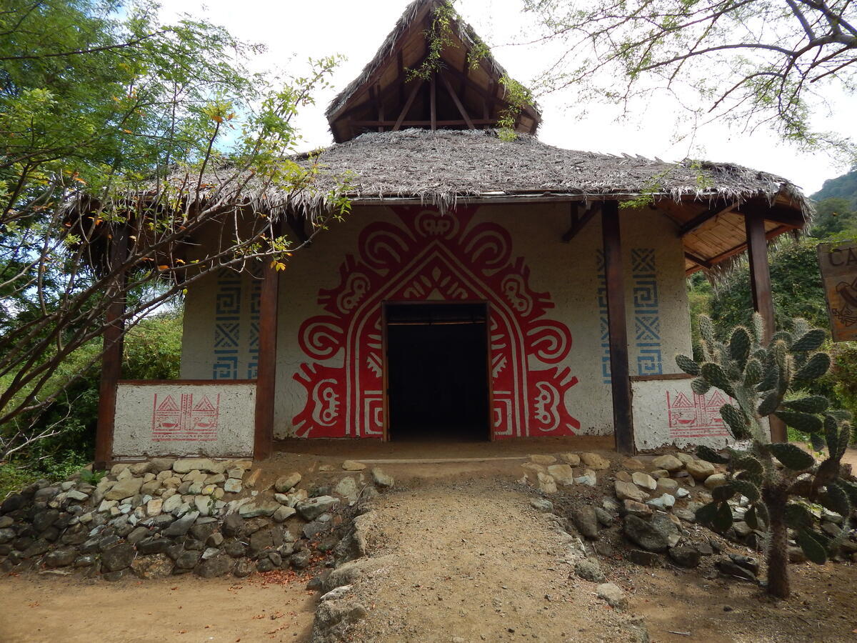 White building with roof made from leaves and red design painted on front