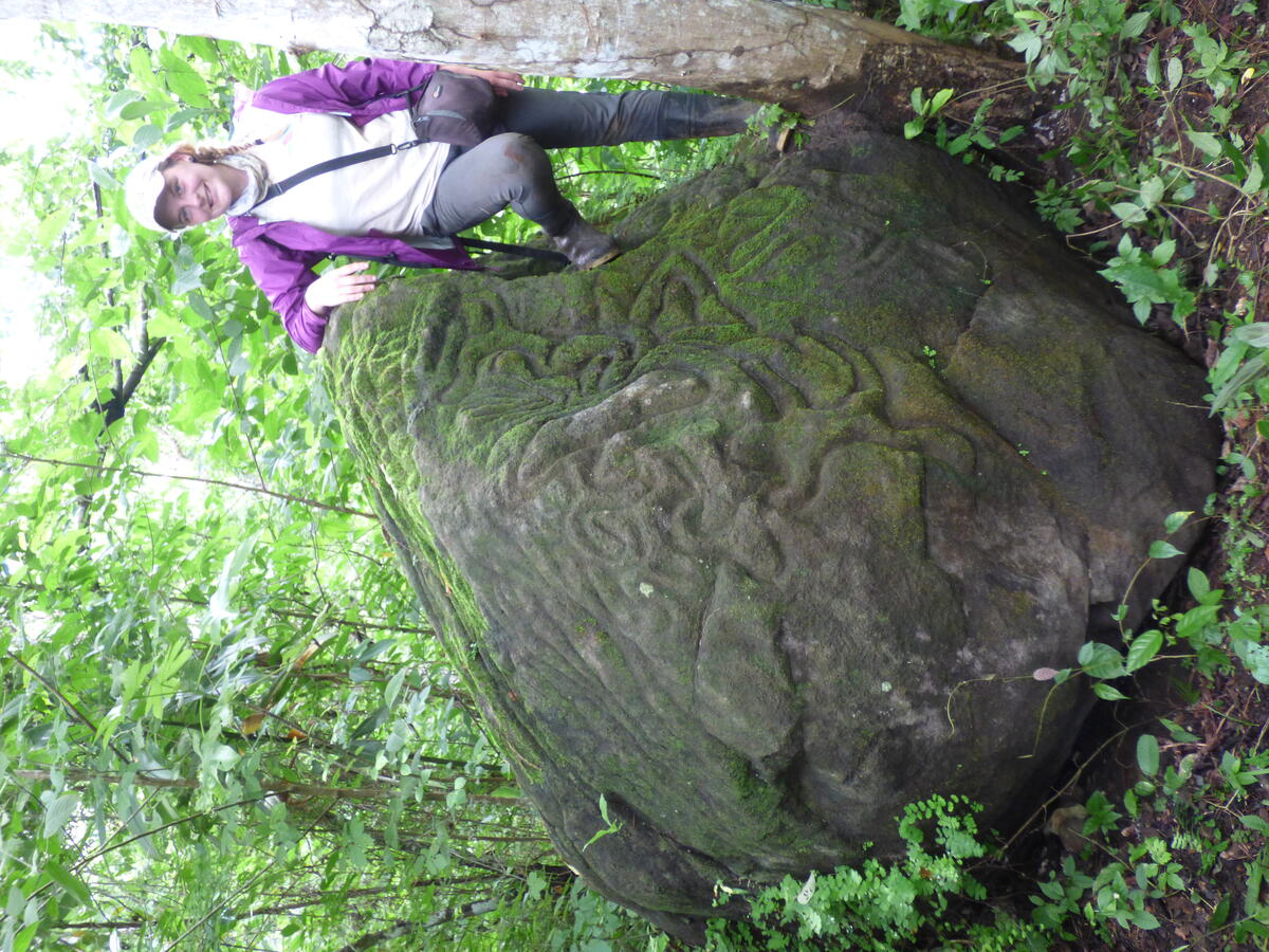 woman standing next to large boulder covered in carvings